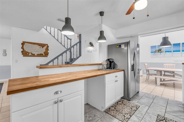 kitchen with stainless steel fridge with ice dispenser, butcher block countertops, ceiling fan, pendant lighting, and white cabinets