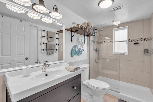 bathroom with toilet, tile patterned flooring, tiled shower, and vanity