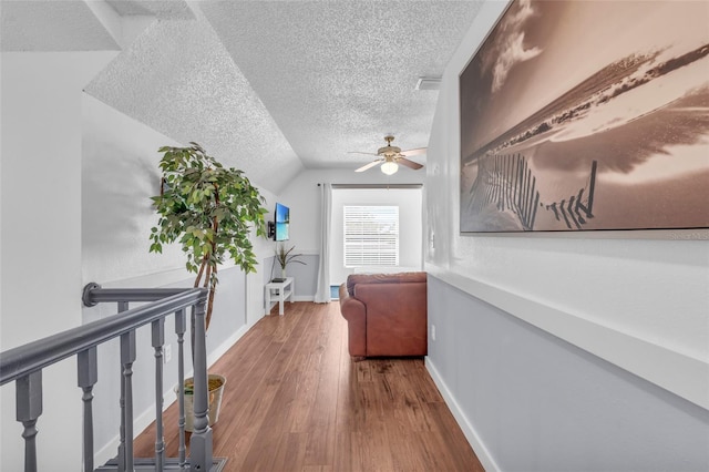 corridor featuring vaulted ceiling, a textured ceiling, and hardwood / wood-style floors