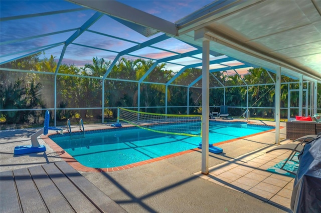 pool at dusk featuring a patio and glass enclosure