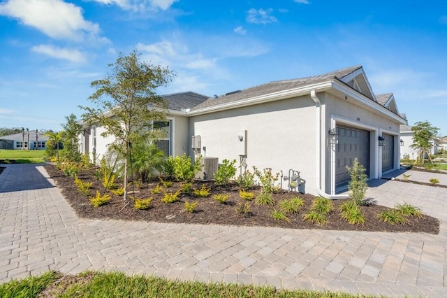 view of home's exterior featuring a garage, central AC unit, decorative driveway, and stucco siding