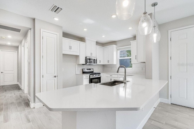 kitchen featuring wood finish floors, stainless steel appliances, light countertops, a sink, and a peninsula