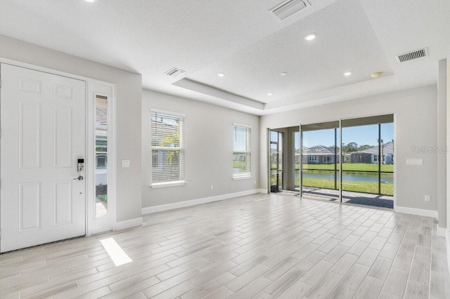 foyer featuring a tray ceiling, light wood-type flooring, and visible vents