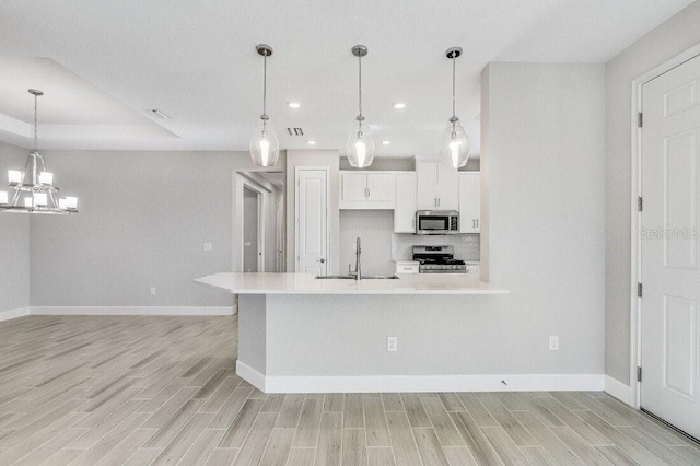 kitchen with appliances with stainless steel finishes, wood tiled floor, light countertops, white cabinetry, and a sink