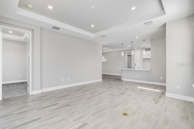 unfurnished living room featuring light wood-style floors, a tray ceiling, and recessed lighting