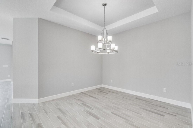 empty room with a raised ceiling, light wood-style flooring, and baseboards