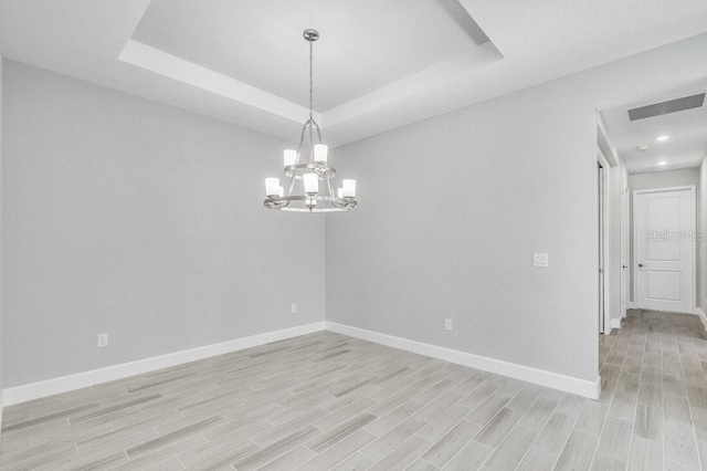 empty room featuring light wood-style floors, a raised ceiling, visible vents, and baseboards