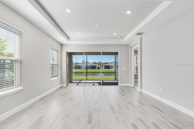 spare room with light wood-style flooring, recessed lighting, visible vents, baseboards, and a raised ceiling