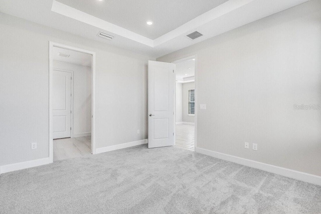 unfurnished bedroom with a tray ceiling, carpet, visible vents, and baseboards