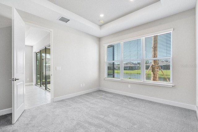 carpeted empty room featuring a tray ceiling, plenty of natural light, visible vents, and baseboards