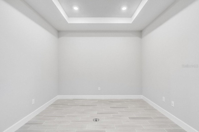 spare room featuring a tray ceiling, light wood-type flooring, and baseboards