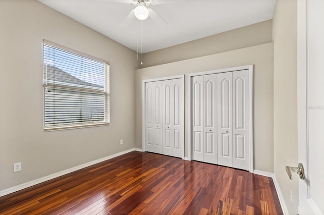 unfurnished bedroom with multiple closets, ceiling fan, and dark hardwood / wood-style floors