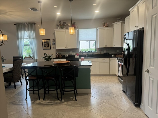 kitchen featuring sink, white cabinetry, decorative light fixtures, a center island, and black refrigerator