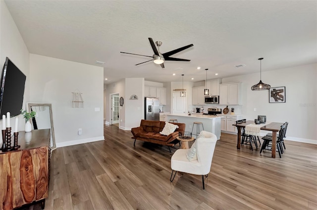 living room with ceiling fan, a textured ceiling, and light hardwood / wood-style floors