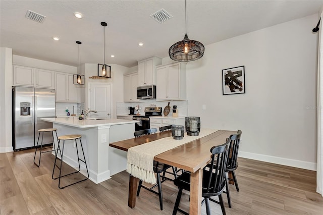 kitchen featuring white cabinets, hanging light fixtures, appliances with stainless steel finishes, and a kitchen breakfast bar