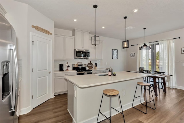 kitchen with decorative light fixtures, white cabinets, stainless steel appliances, and an island with sink