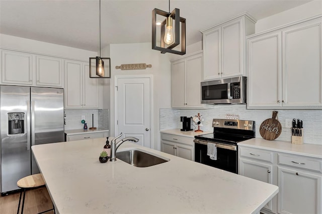 kitchen with decorative light fixtures, backsplash, a center island with sink, sink, and appliances with stainless steel finishes