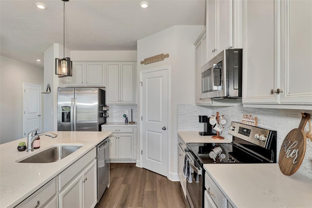 kitchen featuring appliances with stainless steel finishes, decorative light fixtures, dark wood-type flooring, white cabinets, and sink