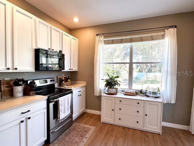 kitchen with light wood-type flooring, white cabinets, and electric stove