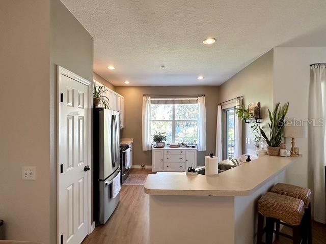 kitchen featuring light hardwood / wood-style floors, a breakfast bar, kitchen peninsula, stainless steel refrigerator, and a textured ceiling