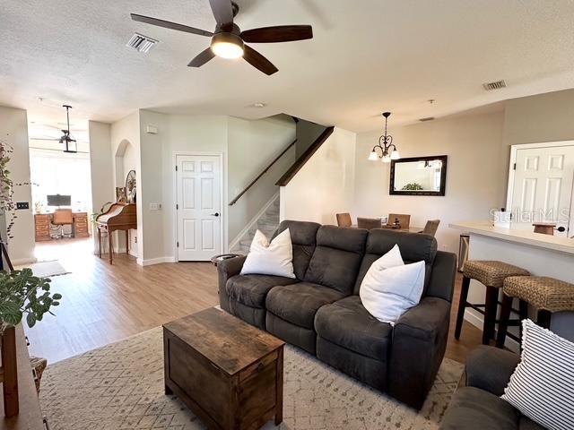 living room featuring ceiling fan with notable chandelier, a textured ceiling, and light hardwood / wood-style flooring