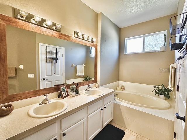 bathroom featuring vanity, tile patterned flooring, a textured ceiling, and tiled tub