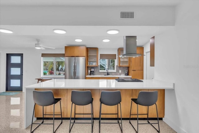 kitchen featuring a kitchen bar, kitchen peninsula, island exhaust hood, stainless steel appliances, and sink