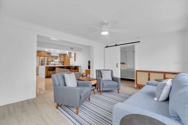 living room featuring ceiling fan, a barn door, and light hardwood / wood-style flooring