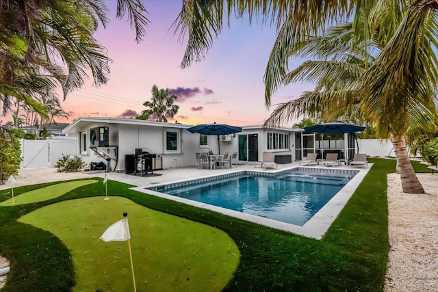 pool at dusk with a patio area and area for grilling