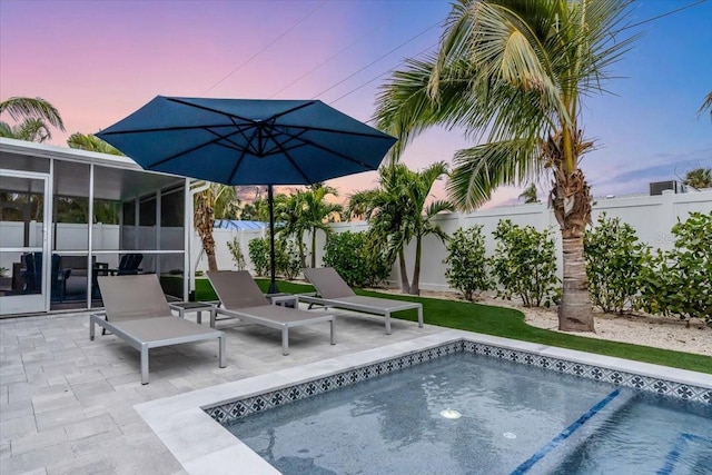 pool at dusk with a sunroom and a patio