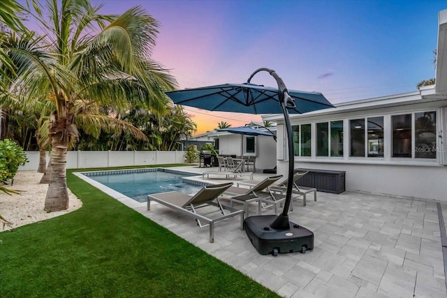 pool at dusk featuring a lawn and a patio