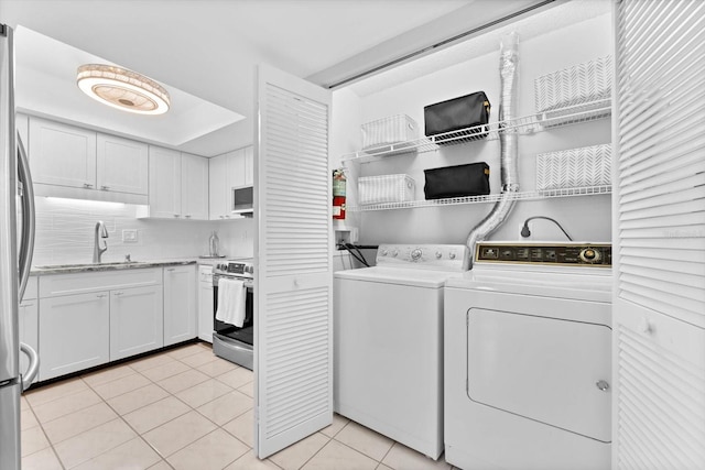 clothes washing area featuring separate washer and dryer, sink, and light tile patterned floors