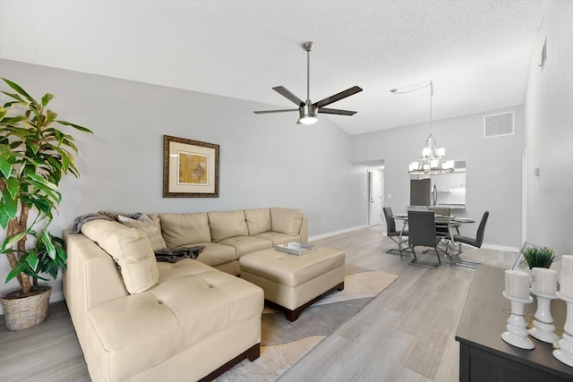 living room with vaulted ceiling, light wood-type flooring, ceiling fan with notable chandelier, and a textured ceiling