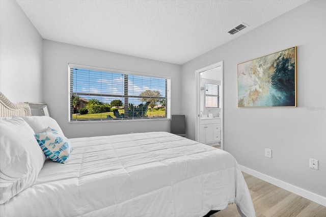 bedroom featuring ensuite bathroom, a textured ceiling, and light wood-type flooring