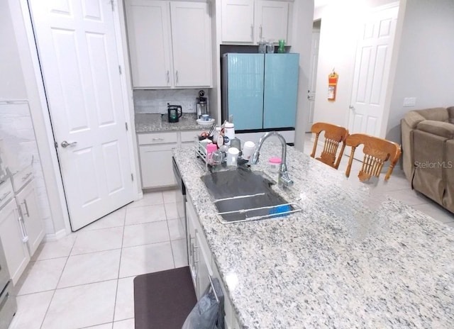 kitchen featuring sink, light tile patterned floors, refrigerator, white cabinetry, and backsplash