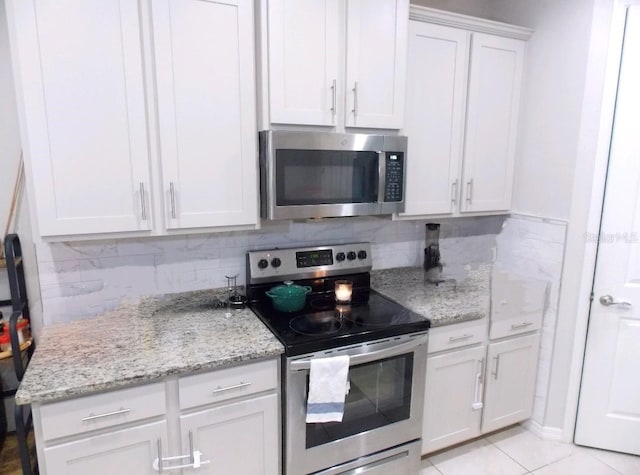 kitchen with light tile patterned floors, appliances with stainless steel finishes, white cabinetry, backsplash, and light stone countertops