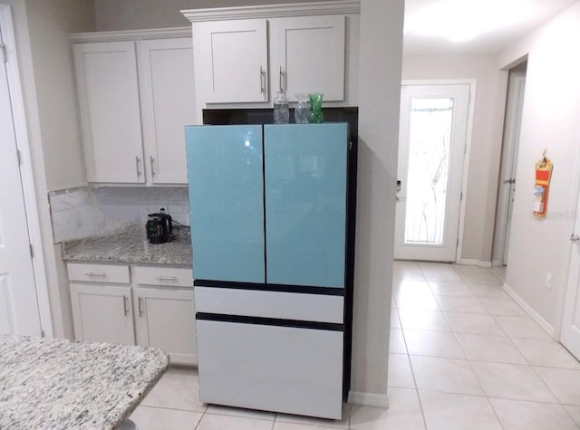 kitchen with fridge, light tile patterned floors, white cabinets, and light stone counters