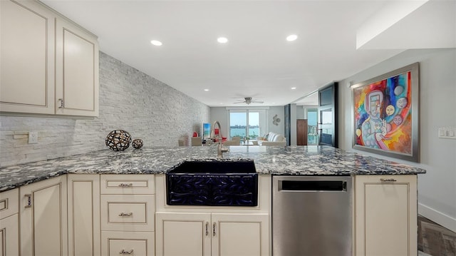 kitchen with dark stone countertops, decorative backsplash, stainless steel dishwasher, and cream cabinetry