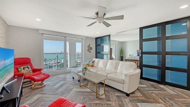 living room with dark parquet floors, ceiling fan, and a water view