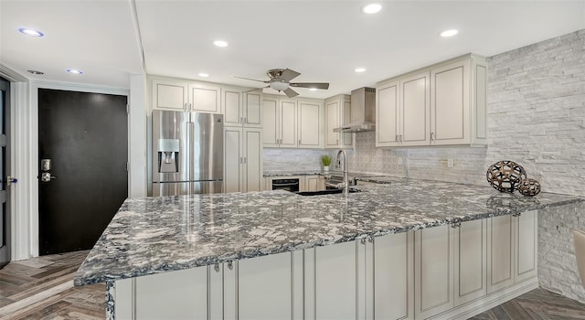 kitchen with sink, stainless steel fridge with ice dispenser, dark stone countertops, kitchen peninsula, and wall chimney range hood