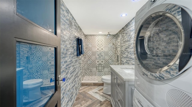 bathroom with stacked washer and dryer, vanity, a shower, parquet flooring, and toilet