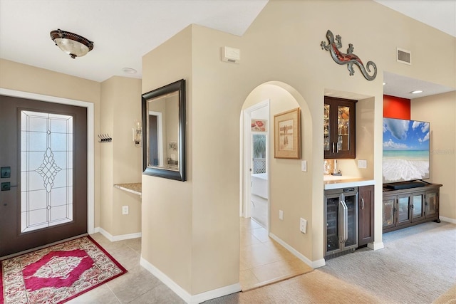 foyer entrance with beverage cooler, a bar, light carpet, and visible vents