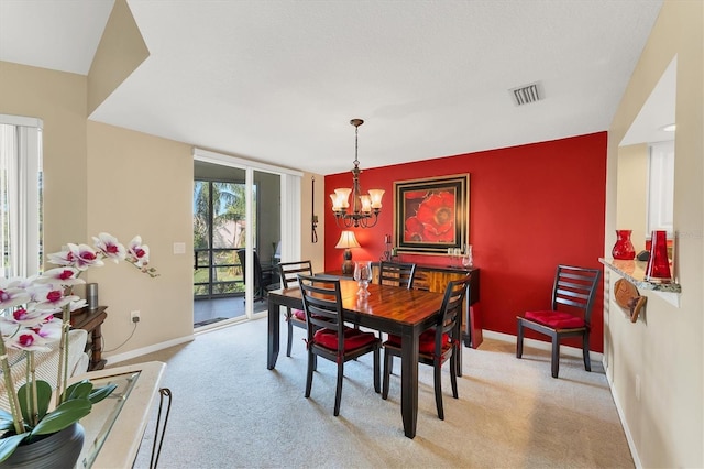 dining area featuring baseboards, visible vents, light colored carpet, an accent wall, and a notable chandelier