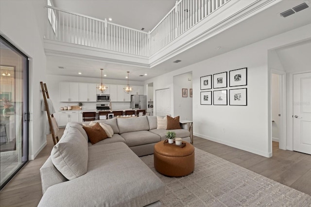 living area featuring a towering ceiling, light wood finished floors, baseboards, and visible vents