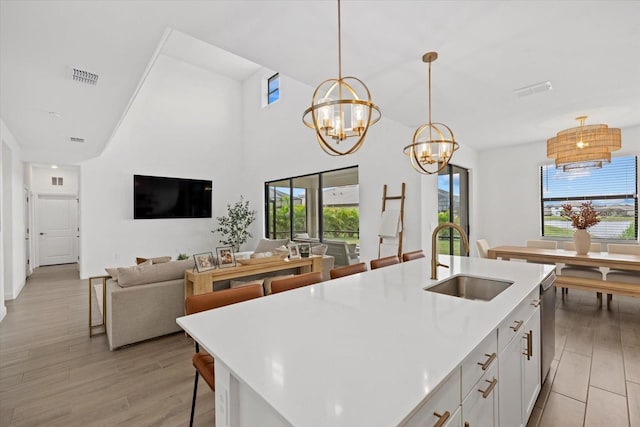 kitchen with sink, white cabinetry, hanging light fixtures, light hardwood / wood-style flooring, and a kitchen island with sink