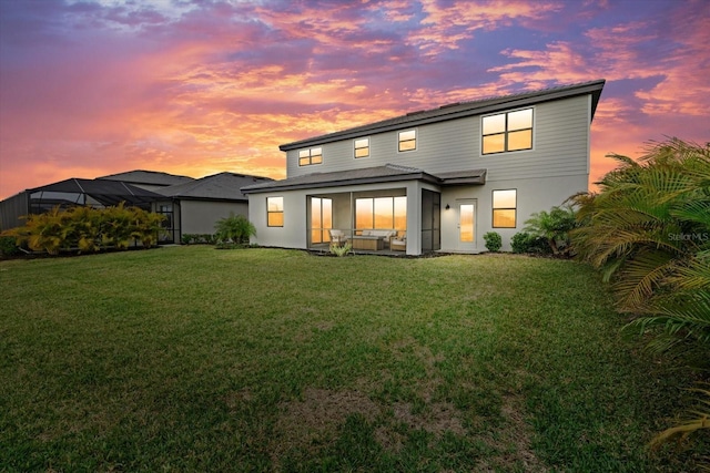 back of house at dusk featuring a lawn