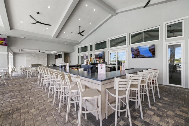 kitchen featuring dark countertops, a ceiling fan, high vaulted ceiling, beamed ceiling, and a kitchen breakfast bar