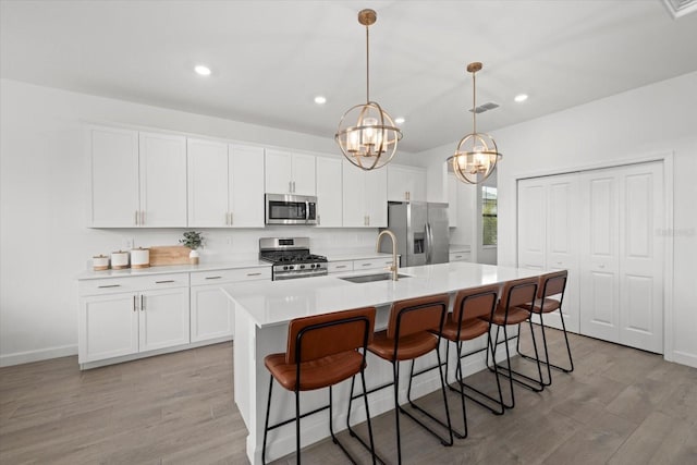 kitchen featuring appliances with stainless steel finishes, decorative light fixtures, a kitchen island with sink, light countertops, and a sink