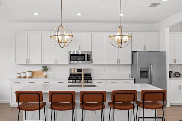 kitchen with appliances with stainless steel finishes, light countertops, an island with sink, and white cabinetry