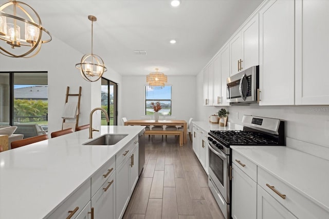 kitchen with white cabinets, wood tiled floor, stainless steel appliances, light countertops, and pendant lighting